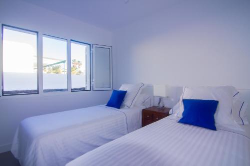 two beds with blue pillows in a room with windows at Rooms & Suites Princesa Leticia in Puerto del Carmen