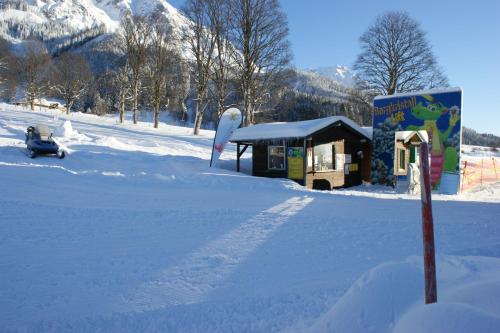 a snow covered road with a small building with a sign at Knollhäusl in Ramsau am Dachstein