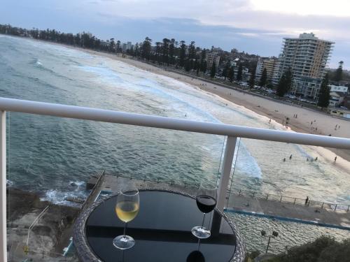 two glasses of wine sitting on a table next to the beach at Manly Waterfront Beach Stay in Queenscliff