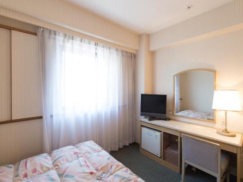 a bedroom with a bed and a desk with a mirror at Tabist Hotel Tetora Kitakyushu in Kitakyushu