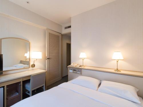 a bedroom with a bed and a desk and a mirror at Tabist Hotel Tetora Kitakyushu in Kitakyushu