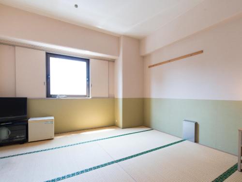 an empty room with a tv and a window at Tabist Hotel Tetora Kitakyushu in Kitakyushu