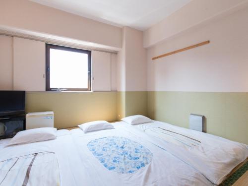 a bedroom with a large white bed with a window at Tabist Hotel Tetora Kitakyushu in Kitakyushu