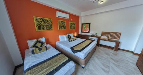 two beds in a room with an orange wall at Mapakada Village - Mahiyanganaya in Mahiyangana