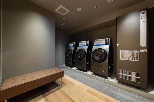 three washing machines in a room with a bench at The OneFive Terrace Fukuoka in Fukuoka