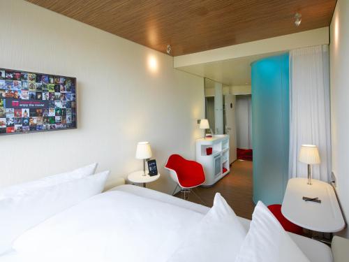 1 dormitorio con 1 cama blanca y 1 silla roja en citizenM Paris Charles de Gaulle Airport en Roissy-en-France
