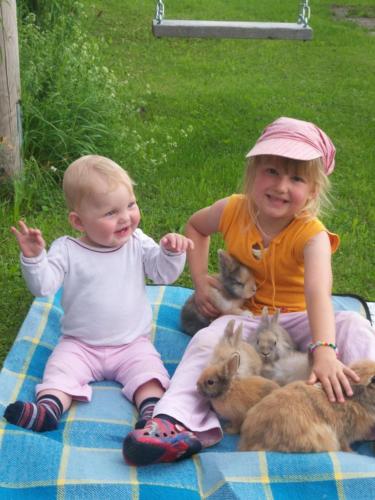 Ein kleines Mädchen und ein Baby auf einer Decke mit Kaninchen in der Unterkunft Irgenbauer in Chieming