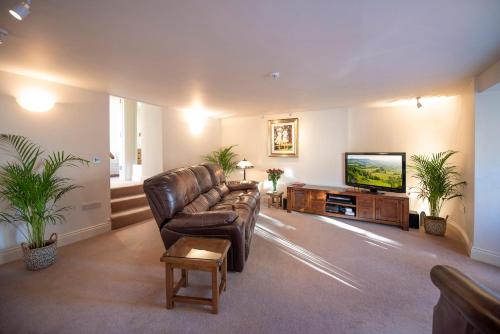 a living room with a leather couch and a flat screen tv at Oberon River View Apartment in Bourton on the Water