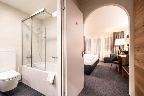 a bathroom with a shower and a toilet and a bed at Alpenhotel Schlüssel in Andermatt