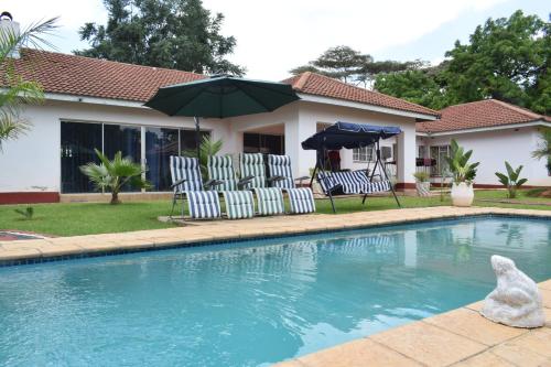 a house with a swimming pool with chairs and an umbrella at The Crown Inn Guest House in Harare