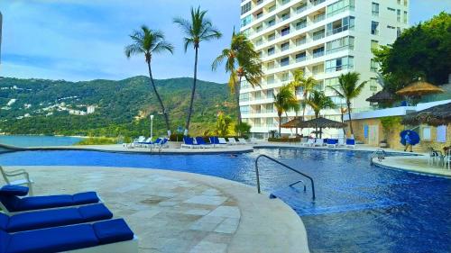 a swimming pool with blue chairs and a building at Departamento con Preciosa Vista al Mar en Acapulco Diamante in Acapulco