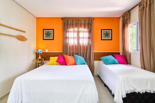 due letti in una stanza con pareti arancioni e cuscini colorati di Casa do Favacho Suítes a Ubatuba