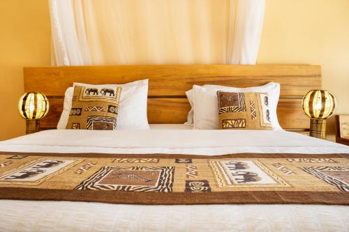 a bed with a wooden headboard and pillows at Kisubi Forest Cottages in Entebbe