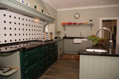 una cocina con armarios verdes y fregadero en Secluded Manor House with pool and tennis court en Bodmin