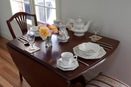 a table with plates and cups and a vase of flowers at Honeyeater Cottage in Seville