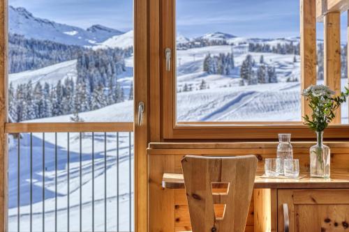 a table with a chair and a view of snow covered mountains at Brunelle Seiser Alm Lodge in Alpe di Siusi