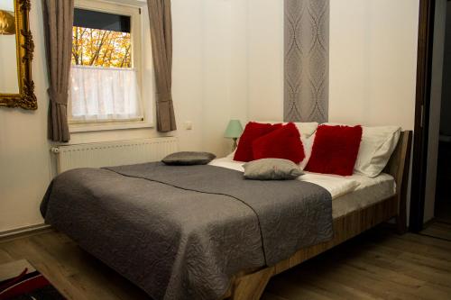 a bedroom with a bed with red pillows and a window at Vadász Panzió és Étterem in Szombathely