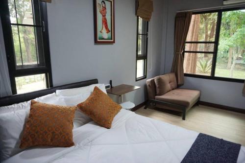 a bedroom with a white bed and a chair and windows at Thanviman Forest Villa Kanjanaburi in Ban Tha Manao