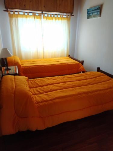 1 dormitorio con 2 camas con sábanas de color naranja y ventana en Departamentos Arco Iris Tandil, en Tandil
