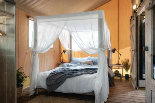 1 dormitorio con cama con dosel y cortinas blancas en Castlemaine Gardens Luxury Safari Tents, en Castlemaine