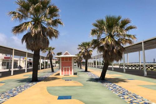 una pasarela con palmeras y un edificio rojo en Barcaresa-LA PERLE VUE MER PIEDS DANS L'EAU CLIM WIFI, en Port Leucate
