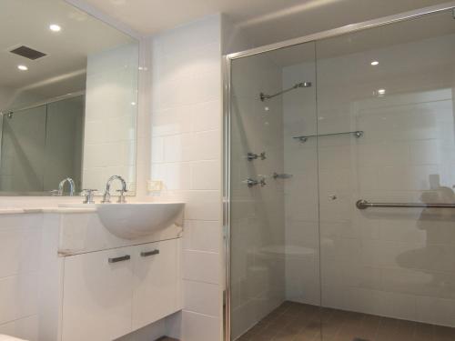a bathroom with a glass shower with a sink and a mirror at Strand Beachside 903 in Forster