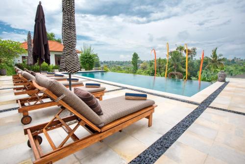 a villa with a pool with chairs and an umbrella at Wake in Paradise and Luxury Lebah Villas in Ubud