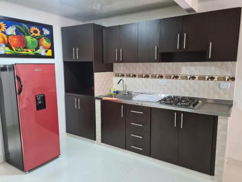 Il comprend une cuisine équipée d'un réfrigérateur rouge et de placards noirs. dans l'établissement Linda y acogedora casa, à Pereira