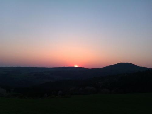 a sunset over a mountain with the sun setting on the horizon at Hotel Eifelstube in Rodder
