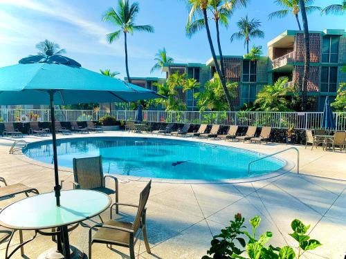 a pool with tables and chairs and an umbrella at Enjoy the sunset at OCEAN FRONT 1BR Apartment - pool on site! in Kailua-Kona