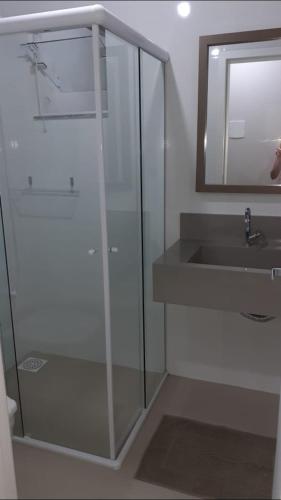 a bathroom with a glass shower and a sink at Apartamento in Bombinhas