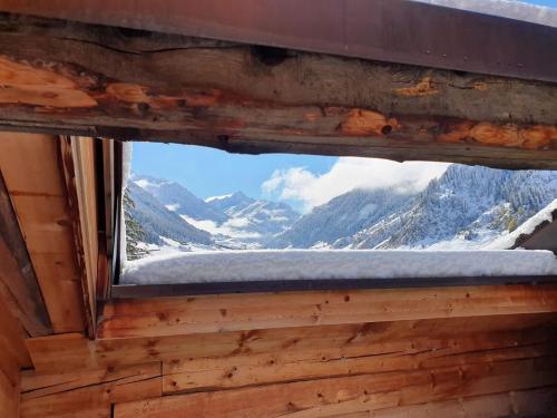 a window in a cabin with a view of a snow covered mountain at Nostalgie Bed & Breakfast Chrämerhus in Curaglia