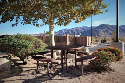 a picnic table and chairs under a tree with mountains at Oasis Inn & Suites 29 Palms Hotel Joshua Tree National Park in Twentynine Palms