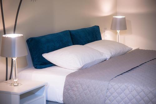 a white bed with a blue pillow and two lamps at Apartamenty Sjesta River in Kudowa-Zdrój