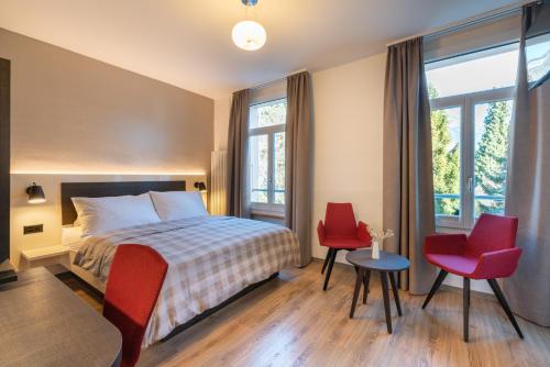 Hotel Derby Interlaken - Action & Relax Hub في إنترلاكن: غرفة نوم بسرير وكرسيين احمر