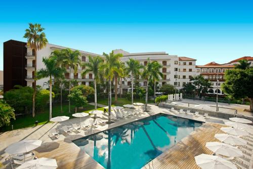 ein Pool mit Stühlen und Sonnenschirmen sowie ein Gebäude in der Unterkunft Iberostar Heritage Grand Mencey in Santa Cruz de Tenerife