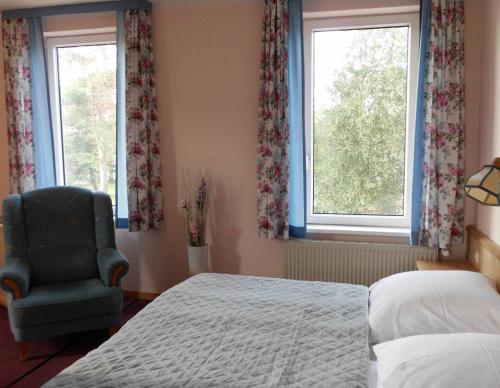 a bedroom with a bed and a chair and two windows at Frühstückspension Landhaus Lange in Prerow