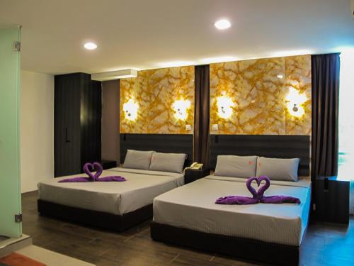 Dos camas en una habitación con toallas púrpuras. en Orchard Inn Puchong en Puchong