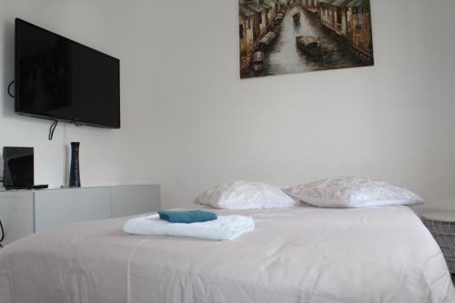 uma cama branca com 2 almofadas e uma televisão de ecrã plano em L4 - Green and cosy flat close Paris - WIFI & NETFLIX em Longjumeau