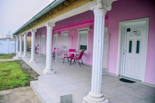 a pink house with white columns and chairs on a porch at Guest House Ceca in Melenci
