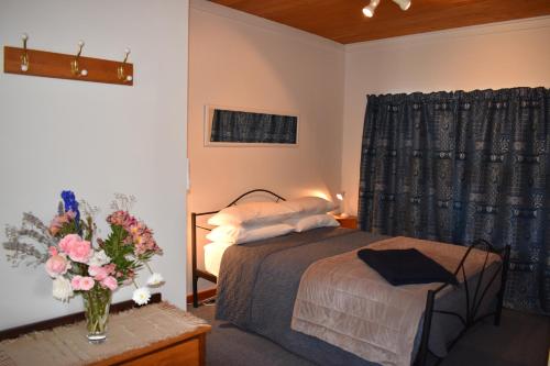 - une chambre avec un lit et un vase de fleurs sur une table dans l'établissement Olivista, à Masterton