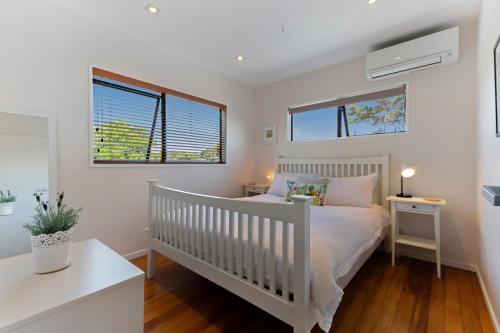 a white bedroom with a crib and two windows at The Cove at Little O in Oneroa