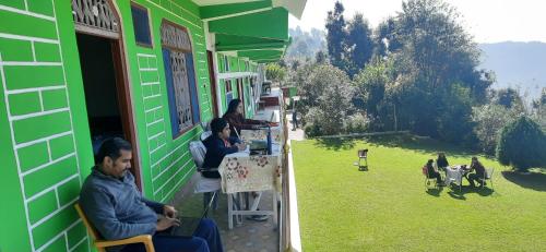 a group of people sitting at tables outside of a green building at Maa Anand Mayee Guest House in Panuānaula