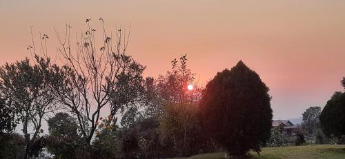 a sunset over a field with trees and a house at Maa Anand Mayee Guest House in Panuānaula