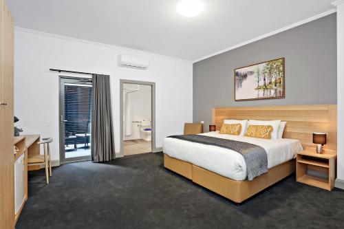 a bedroom with a bed and a desk and a bathroom at Meridian Hotel Hurstville in Sydney