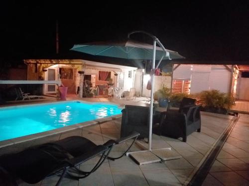 a pool at night with chairs and an umbrella at Studio avec piscine partagee jardin clos et wifi a Les Abymes in Les Abymes