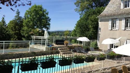 a swimming pool with chairs and umbrellas next to a house at Bungalow de 3 chambres avec piscine partagee terrasse amenagee et wifi a Argences en Aubrac in Banes