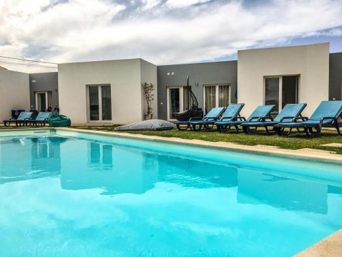 a swimming pool with blue chairs next to a house at 4 bedrooms house with shared pool enclosed garden and wifi at Atalaia 3 km away from the beach in Lourinhã