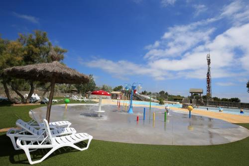 un parque acuático con piscina con sillas y sombrilla en Camping Campéole La Côte des Roses - Maeva en Narbona