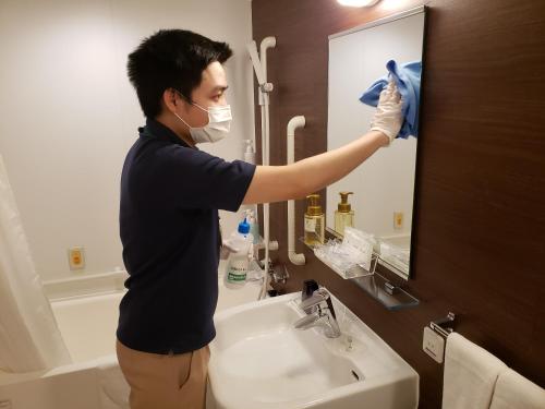 Ein maskierter Mann, der im Bad einen Spiegel putzt. in der Unterkunft Quad Inn Yokote in Yokote